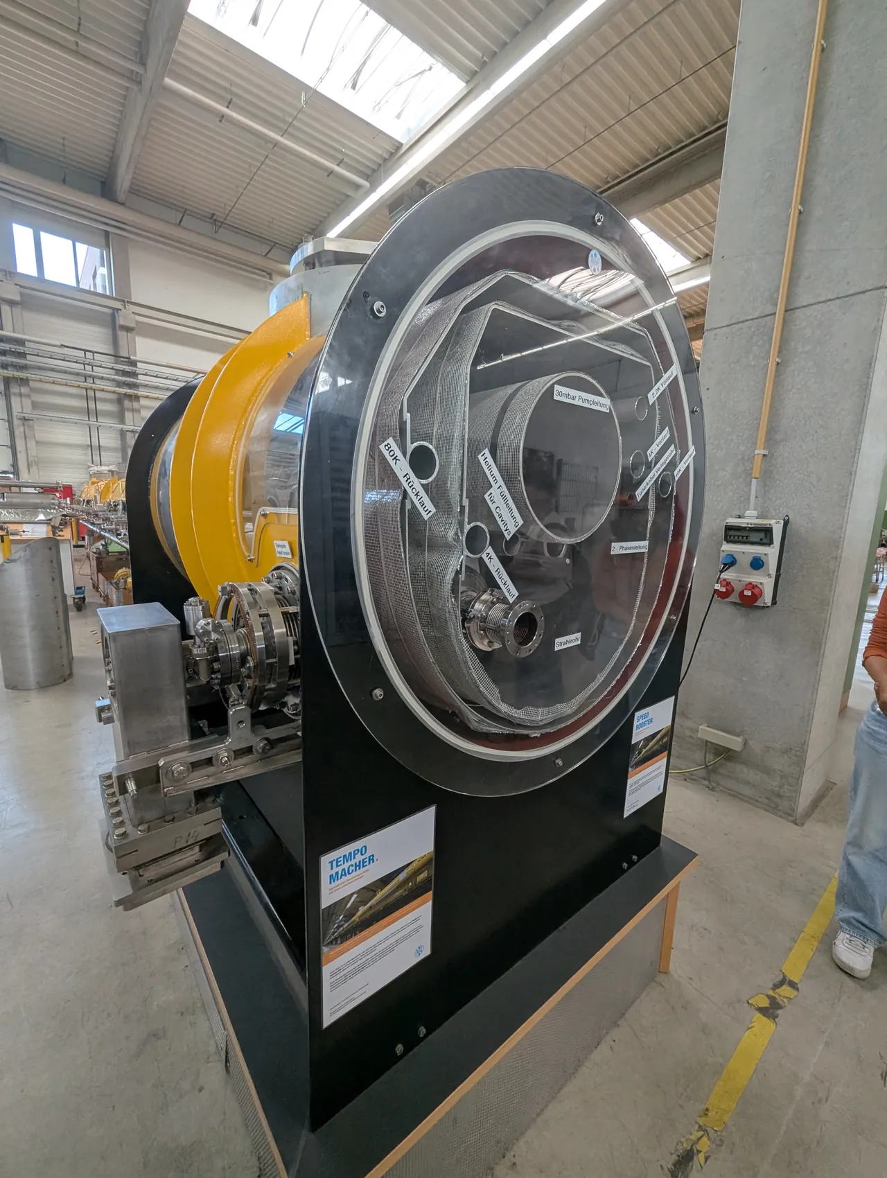 A cut-open accelerator magnet on display in a hall at DESY, its yellow coil and layered steel rings visible behind a clear cover.